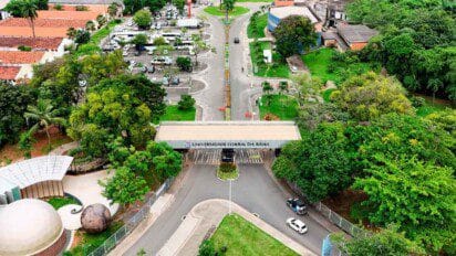 Vista aérea da entrada principal da Universidade Federal da Bahia - UFBA, com portaria, árvores ao redor e área de estacionamento ao fundo.