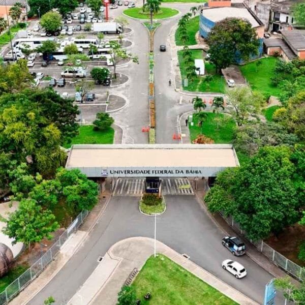 Vista aérea da entrada principal da Universidade Federal da Bahia - UFBA, com portaria, árvores ao redor e área de estacionamento ao fundo.