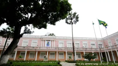 Fachada do prédio histórico da Universidade Federal do Ceará, com paredes rosadas, jardim frontal, árvores e bandeiras hasteadas. Foto: Divulgação/UFC