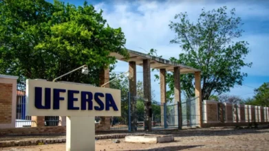 Entrada do campus da UFERSA com placa institucional em destaque, portão de colunas ao fundo e árvores ao redor sob céu azul. Foto: Divulgação/UFERSA