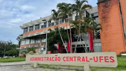 Prédio da Administração Central da UFES com fachada em tijolos, palmeiras na frente e placa com o nome Administração Central UFES em letras vermelhas. Foto: Divulgação/UFES