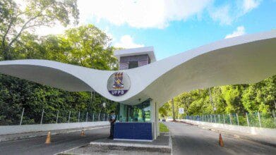 Portaria principal da UFPB com estrutura moderna em concreto branco, logotipo da universidade ao centro e área cercada por árvores. Foto: Divulgação/UFPB