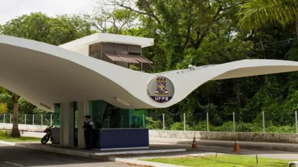 UFPB abre concurso com 30 vagas imediatas e salários de até R$ 14,3 mil 4 Entrada principal da Universidade Federal da Paraíba com guarita branca de arquitetura curva, brasão da UFPB ao centro e área arborizada ao redor. Foto: Divulgação/UFPB