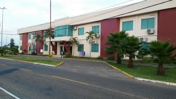 Prédio administrativo da Universidade Federal de Roraima com fachada em tons claros e vermelho, janelas verdes, palmeiras na frente e acesso pela via interna do campus. Foto: Divulgação/Google Maps (Micky Brian)