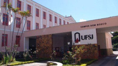 Fachada do Campus Dom Bosco da UFSJ com prédio de janelas vermelhas, jardim e letreiro com o logotipo da universidade. Foto: Divulgação/UFSJ