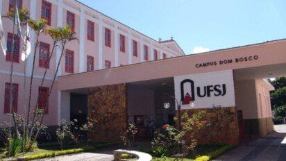 Fachada do Campus Dom Bosco da UFSJ com prédio de janelas vermelhas, jardim e letreiro com o logotipo da universidade. Foto: Divulgação/UFSJ
