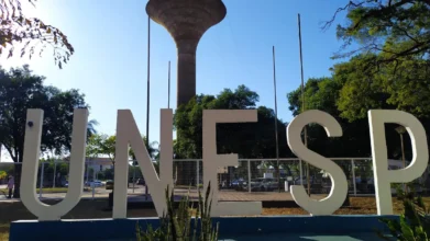Letreiro da UNESP em primeiro plano, com letras brancas grandes, árvores ao redor e uma torre de água ao fundo sob céu azul. Foto: Divulgação/Governo do Estado de São Paulo
