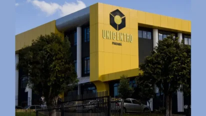 Fachada de prédio moderno com estrutura amarela e preta, exibindo o logotipo e o nome UNICENTRO Paraná em letras metálicas, cercada por árvores e uma grade frontal sob céu azul claro