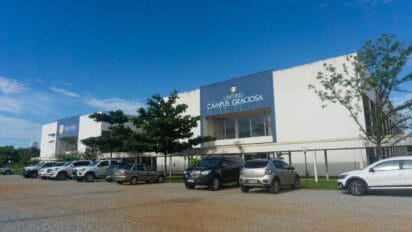 Fachada do UNITINS Câmpus Graciosa com estacionamento em frente e vários carros estacionados sob céu azul com poucas nuvens.