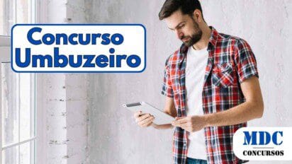 Homem de barba, cabelo curto e pele clara usa uma camisa xadrez vermelha sobre uma camiseta branca enquanto segura e olha para um tablet em um ambiente iluminado - Umbuzeiro PB oferece 178 vagas e salários de até R$ 3,7 mil em Concurso