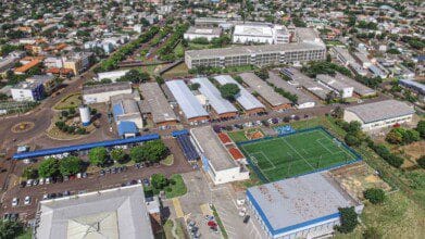 Vista aérea de um campus universitário da Unioeste Cascavel com prédios, estacionamentos, área verde e um campo de futebol cercado por rede. Foto: Divulgação/Unioeste